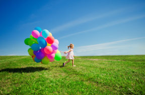 Happy little girl holding colorful balloons. Child playing on a